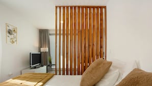 A bedroom with a bed, a television on a nightstand, a wooden partition, and a framed picture on the wall.