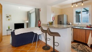 A compact kitchen with a dining area, a TV, and a view of the sea.