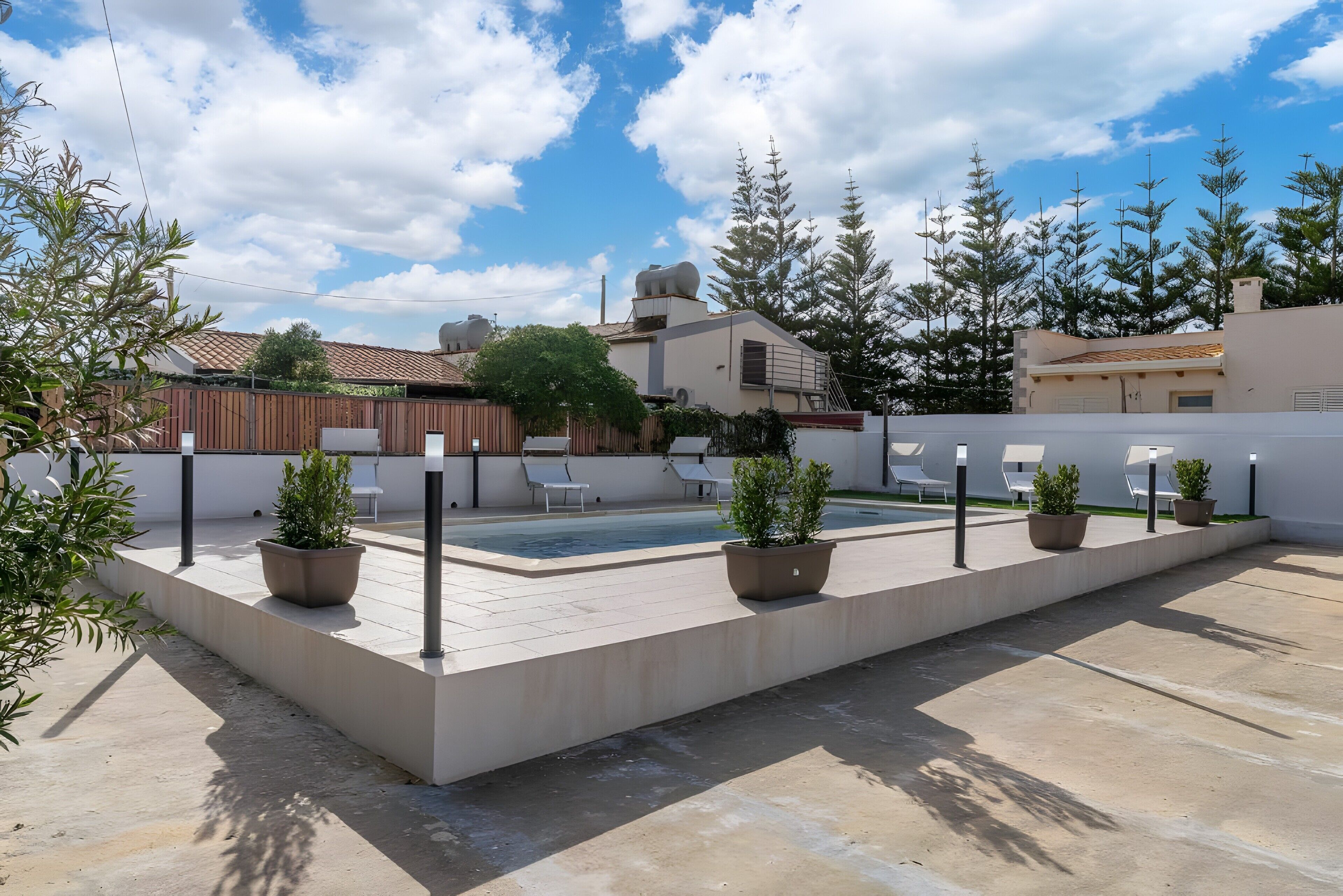 Área de piscina en la azotea con plantas en macetas, mobiliario exterior y cielo despejado.