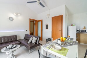 Uma sala de estar moderna com sofá, mesa de jantar com cadeiras, área de cozinha e ventilador de teto.