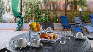 Un espacio al aire libre cubierto con una mesa preparada para el desayuno, con pasteles y fruta, y dos sillones de relax.