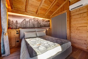 Une chambre dans une cabane en bois, avec un lit, une fenêtre donnant sur une forêt et un appareil de climatisation.
