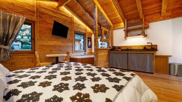 Een houten blokhut van binnen met een bed, een tafel, een stoel, een keukenhoek en een aan de muur bevestigde televisie.