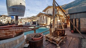 A rustic outdoor setting with a large wooden barrel, a wooden structure, and a house in the background. - Studio 'Con Idromassaggio' with Mountain View, Balcony and Wi-Fi (Aymavilles)