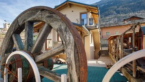 A rustic building with large wooden wheels, a balcony, and a mountain backdrop. - Studio 'Con Idromassaggio' with Mountain View, Balcony and Wi-Fi (Aymavilles)