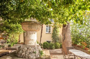 A courtyard with a stone fountain, a bench, and a table under a tree.