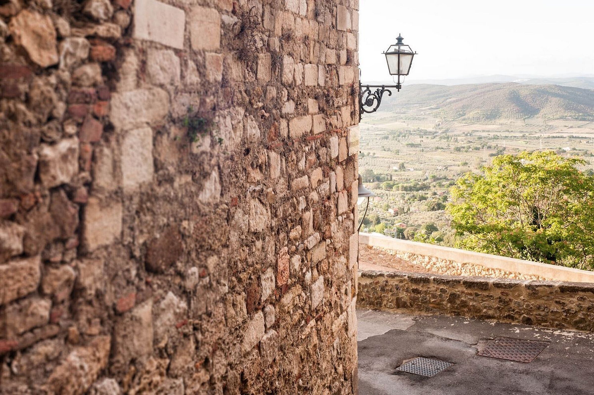 A stone wall with a street lamp and a view of a valley.