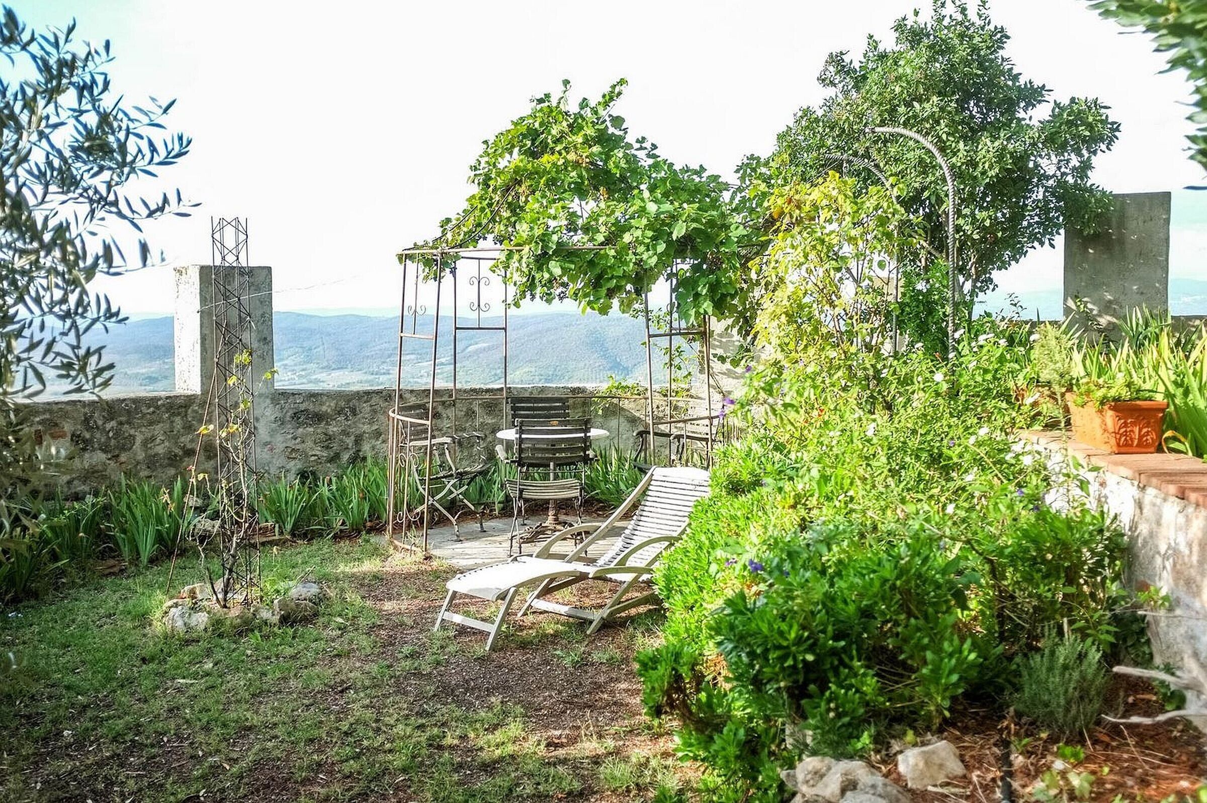 A garden with a pergola, two lounge chairs, and a view of the sea.