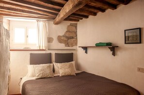 A bedroom with a bed, a stone wall, a window with curtains, and a shelf with a green object.