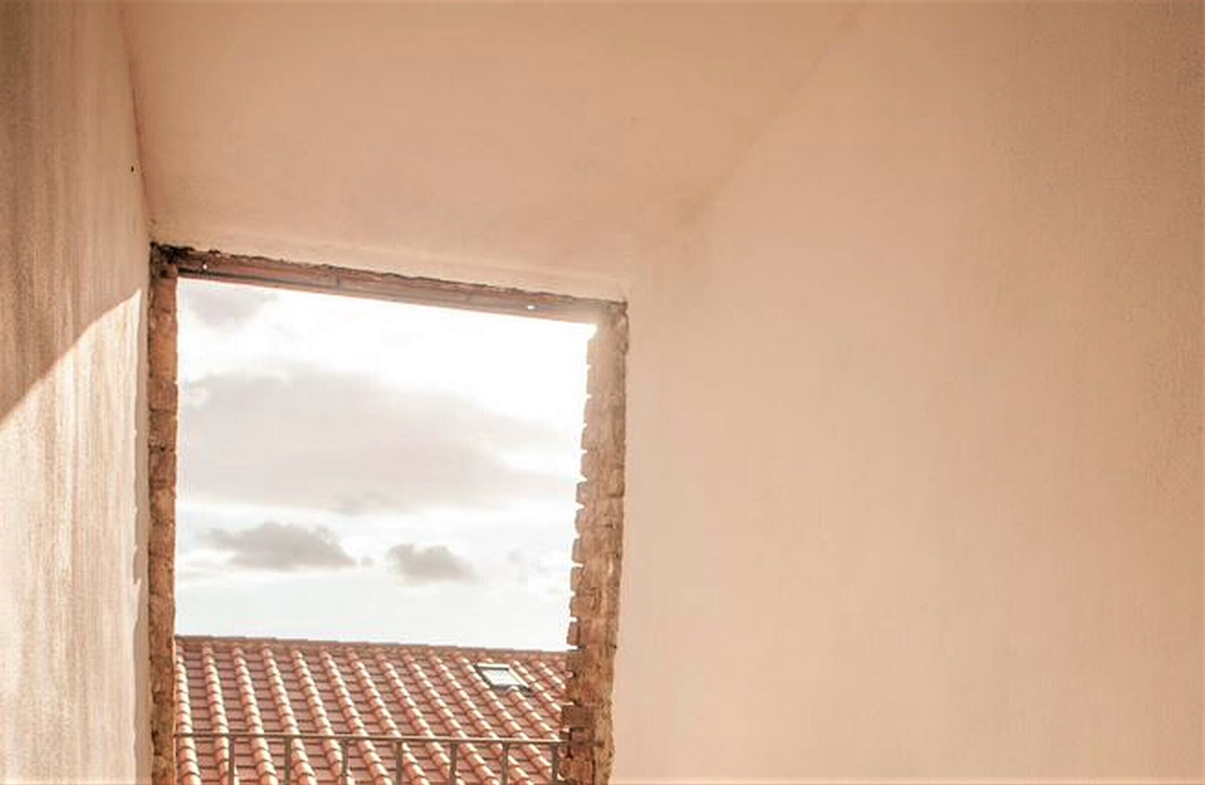 A room with a sloped ceiling, a window with a view of a tiled roof, and a partial view of a wall.