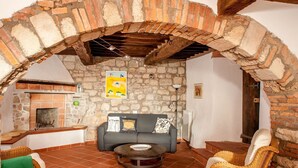 Un espacio de estar acogedor con pared de piedra, chimenea, sofá y muebles de mimbre.