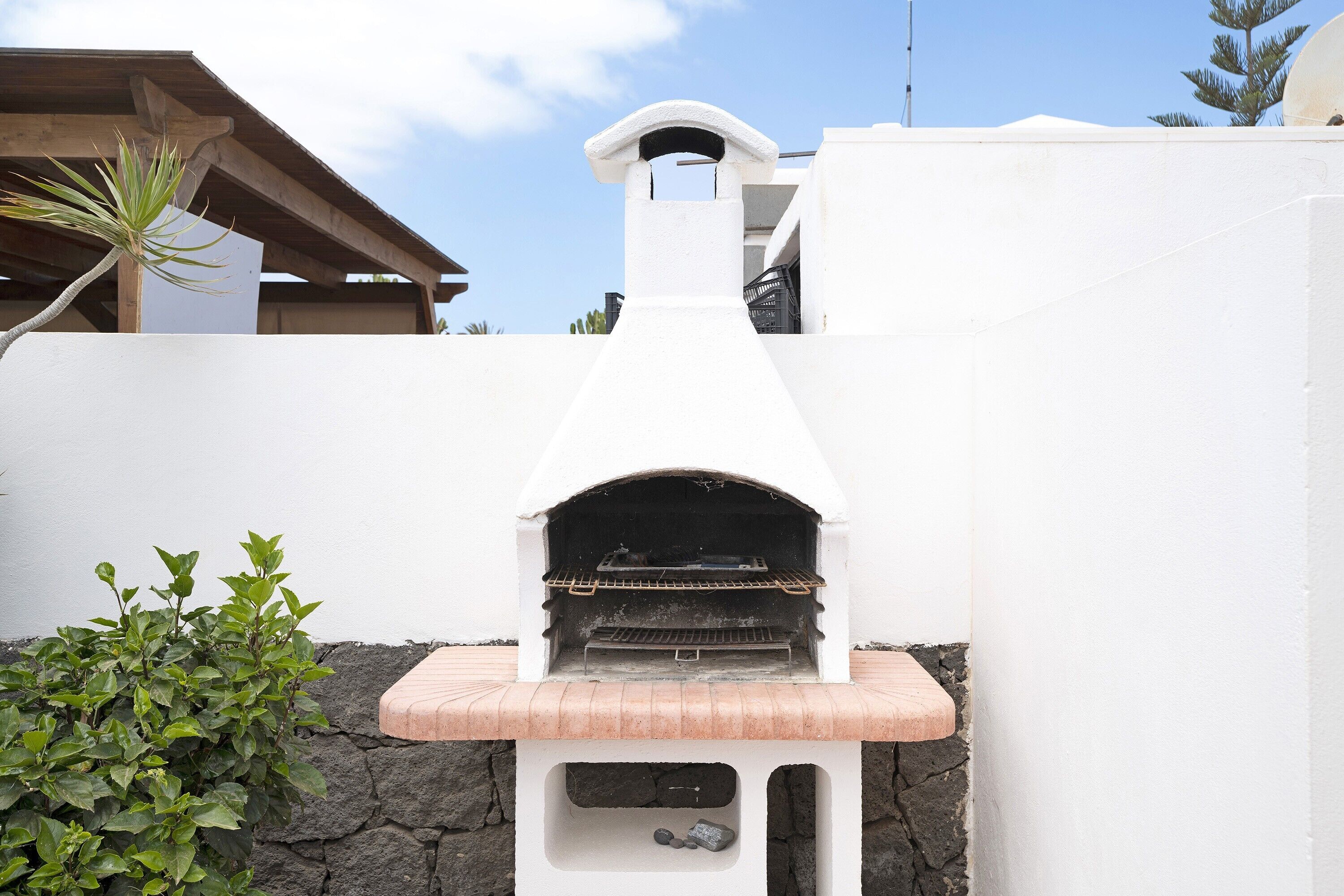 A stone wall with a white structure, possibly a barbecue area, and a plant to the left.