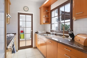 Una cocina con armarios de madera, un lavabo, un ventanal y un reloj en la pared.