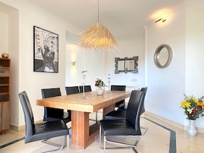 A dining area with a wooden table, black chairs, a hanging light fixture, a framed picture, a mirror, and a vase with flowers. - Holiday Home 'Sunset Bay' with Sea View, Wi-Fi and Air Conditioning (Illes Balears)