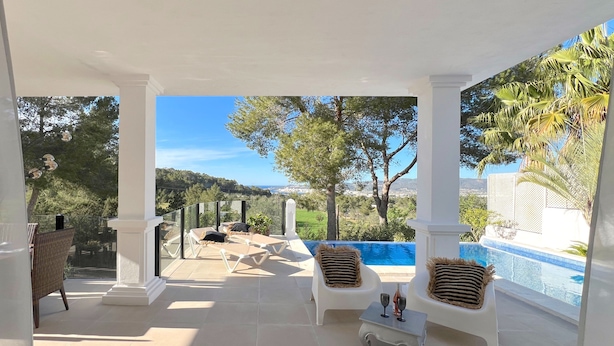 Un espace extérieur aménagé, abrité et doté de sièges, avec une piscine, des colonnes blanches et une vue sur le paysage.
