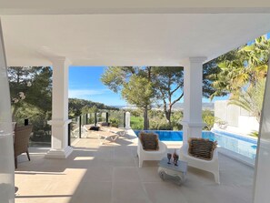 Un espace extérieur aménagé, abrité et doté de sièges, avec une piscine, des colonnes blanches et une vue sur le paysage.