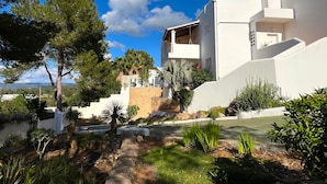 Un bâtiment moderne aux murs blancs, doté d’une base en pierre, et entouré d’une végétation luxuriante et d’arbres.