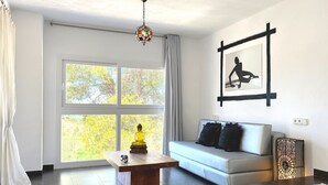 Un salon moderne avec un canapé, une table basse, une statue de Bouddha et une grande fenêtre donnant sur la forêt.