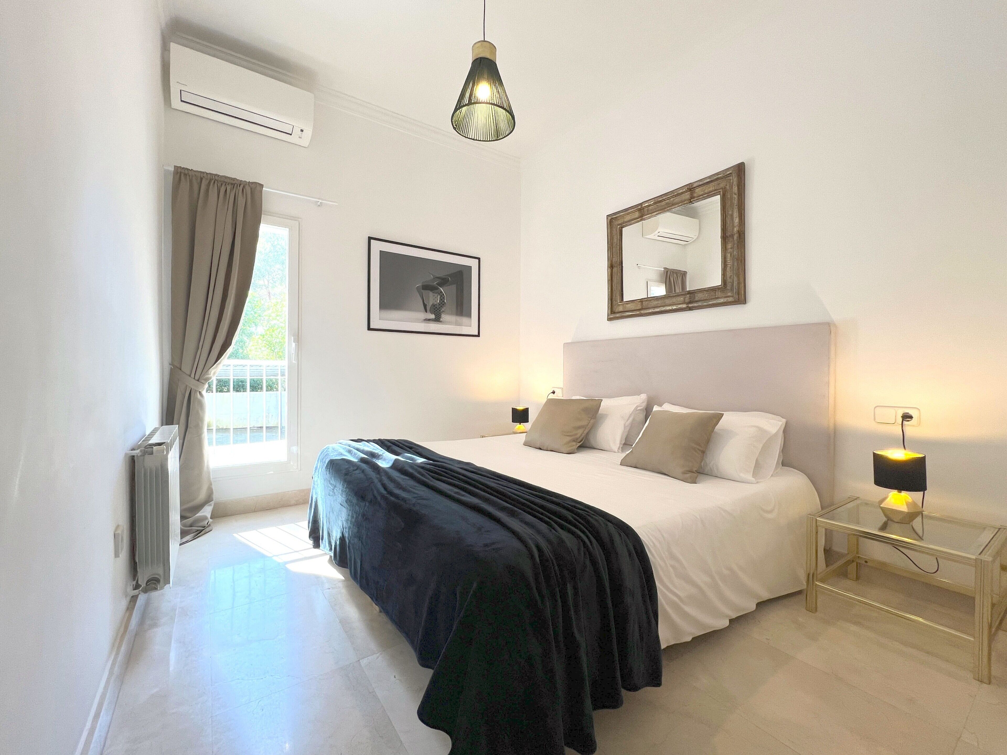 Une chambre à coucher comprenant un lit, des lampes de chevet, une fenêtre avec des rideaux, un radiateur et un luminaire au plafond.