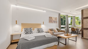 Moderni hotellihuone, jossa on sänky, sohva, ruokapöytä ja näkymä ulos.