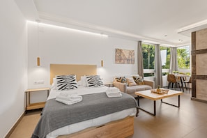 Quarto de hotel moderno com cama, sofá, mesa de jantar e vista para o exterior.