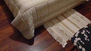 Una cama bien hecha con una colcha acolchada, una mesita de noche con lámpara, un radiador y una alfombra estampada en el suelo.