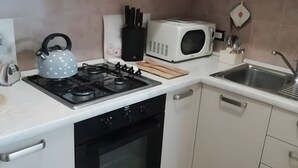 Una cocina con armarios blancos, estufa a gas, microondas y un lavabo.
