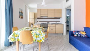 A modern kitchen with wooden cabinets, a dining table with chairs, and a blue sofa with a colorful pillow. - Apartment 'Ammari' with Private Terrace, Balcony and Air Conditioning (Marina di Ragusa)