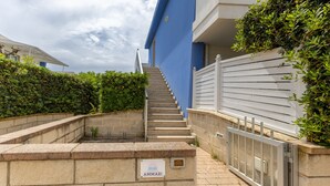 A staircase leading to a building with a blue exterior, a stone wall with a sign, and a metal gate. - Apartment 'Ammari' with Private Terrace, Balcony and Air Conditioning (Marina di Ragusa)