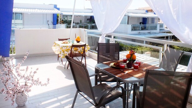 A balcony with a table set for breakfast, chairs, a potted plant, and a view of the city. - Apartment 'Ammari' with Private Terrace, Balcony and Air Conditioning (Marina di Ragusa)