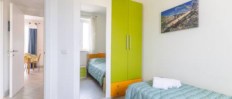 Un dormitorio con dos camas, un armario verde, un cuadro en la pared y una zona de comedor al fondo.