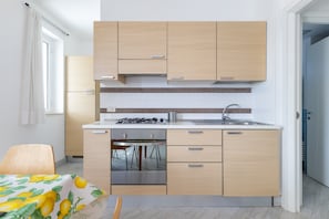 A modern kitchen with light wood cabinets, a stainless steel sink, and a built-in oven.