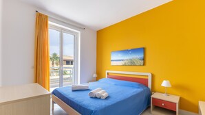 A hotel room with a bed, a nightstand, a lamp, a painting, and a view of the outside. - Apartment 'Ammari' with Private Terrace, Balcony and Air Conditioning (Marina di Ragusa)