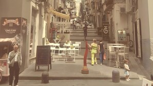 Une rue étroite, bordée de bâtiments des deux côtés, un homme se tenant près d’un étal de nourriture et un enfant qui marche.