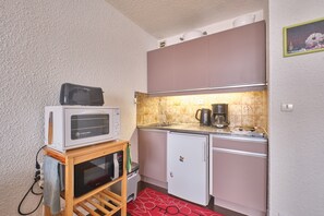 Una cocina compacta con microondas, cafetera y un refrigerador pequeño.