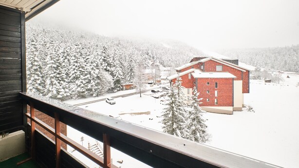 A view from a window overlooking a snow-covered landscape with a red building and a wooden balcony.