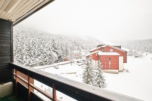 A view from a window overlooking a snow-covered landscape with a red building and a wooden balcony.