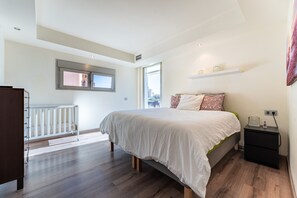 A bedroom with a bed, a nightstand, a window, and a crib.