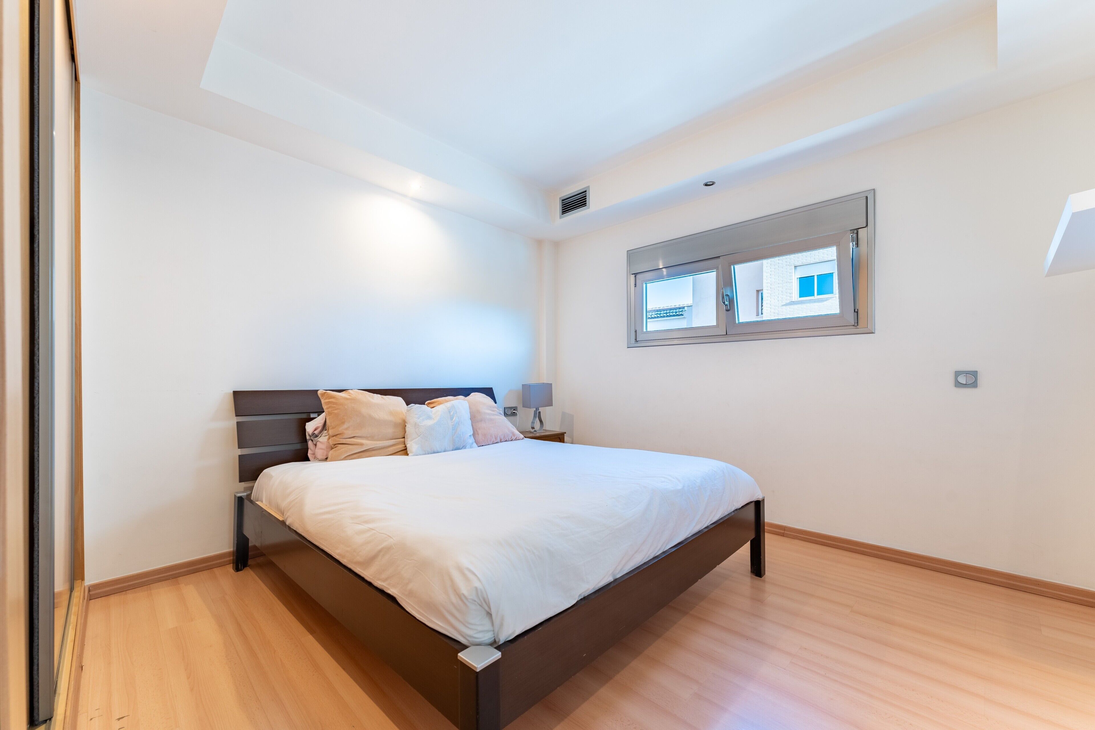 A bedroom with a bed, nightstand, lamp, window, and wooden flooring.
