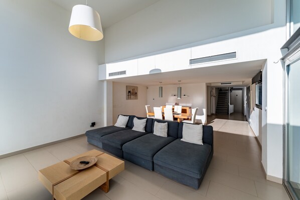 A modern living room with a sectional sofa, a wooden coffee table, and pendant lighting.