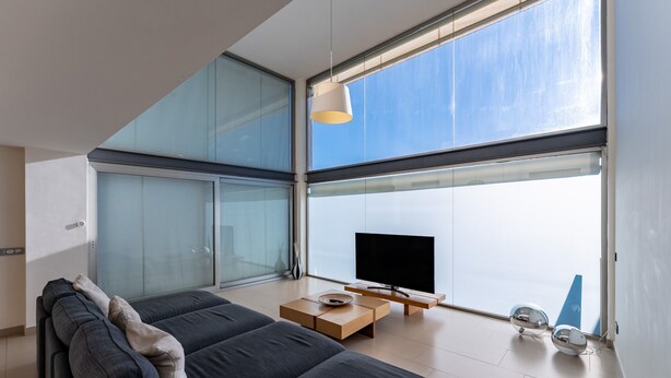 Een moderne woonkamer met een grote televisie, een bank, een salontafel en uitzicht door grote ramen.