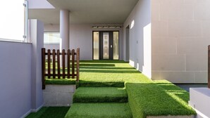 Een modern gebouw met een betonnen gevel, een houten hek en een pad met kunstgras.