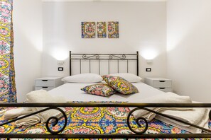 Un lit avec un cadre en métal, une literie blanche et des coussins décoratifs. Il y a deux tables de chevet avec des lampes.