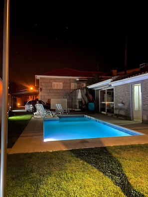 Une piscine avec une terrasse carrelée, un patio couvert et un bâtiment en pierre en arrière-plan.