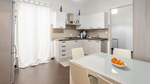 Una cocina moderna con armarios blancos, una mesa de comedor con sillas y un bol de naranjas sobre la mesa.