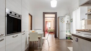 Una cocina moderna con armarios blancos, horno empotrado, comedor con mesa y sillas y refrigerador.