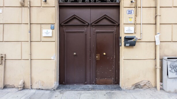 Una puerta doble con un arco de metal encima, una caja de servicios y una placa con un número de casa.