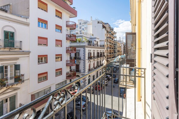 Un edificio de varios pisos con balcones, vista a la calle y automóviles estacionados.