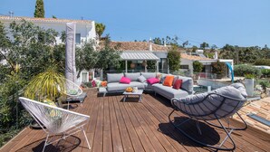 Een houten terras met buitenmeubilair, waaronder een loungeset en stoelen, en een eettafel.