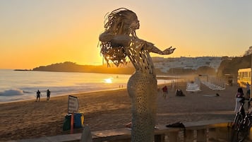 A sculpture of a mermaid on a beach with a sunset in the background.